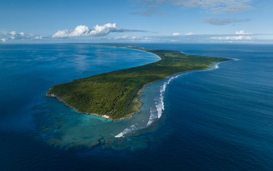 Aerial view of the island s lush greenery meeting the turquoise waters with white waves crashing against the shore Ouvéa Loyalty Islands Province New Caledonia. Aerial view of the island s lush greenery meeting the turquoise waters with white waves crashing against the shore Ouvéa Loyalty Islands Province New Caledonia.