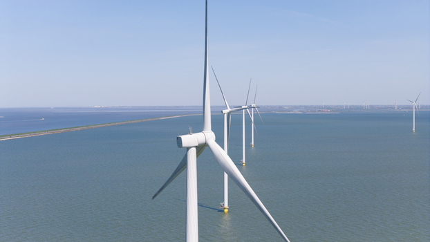 Aerial view of Windpark Fryslan wind turbines standing in the water of the IJsselmeer with a dike visible in the background in Breezanddijk Friesland Netherlands. Aerial view of Windpark Fryslan wind turbines standing in the water of the IJsselmeer with a dike visible in the background in Breezanddijk Friesland Netherlands.