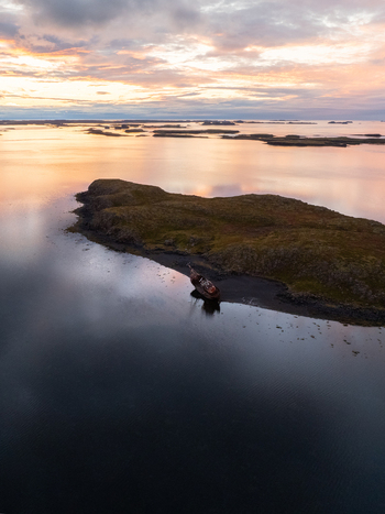 Aerial view of a small island with a shipwreck the sky ablaze in pastel hues reflecting on the calm waters surrounding the rugged landscape Snæfellsnes Eyja og Miklaholtshreppur Iceland. Aerial view of a small island with a shipwreck the sky ablaze in pastel hues reflecting on the calm waters surrounding the rugged landscape Snæfellsnes Eyja og Miklaholtshreppur Iceland.