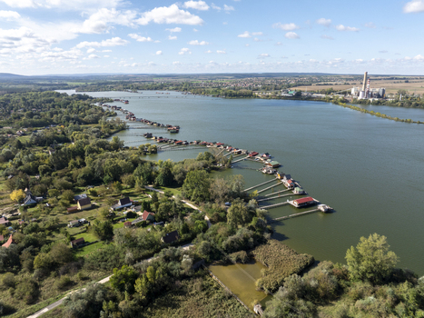 Aerial view of Bokodi Floating Village with its iconic colorful wooden houses on stilts over the lake surrounded by lush greenery and a distant power plant in Oroszlany Hungary. Aerial view of Bokodi Floating Village with its iconic colorful wooden houses on stilts over the lake surrounded by lush greenery and a distant power plant in Oroszlany Hungary.