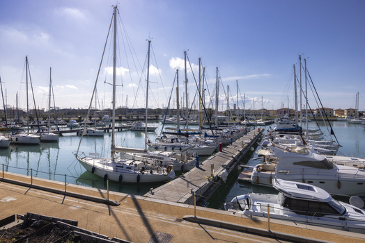 View of sailboats and motorboats docked at the harbor piers under a clear blue sky in Marina di Pisa Tuscany Italy.