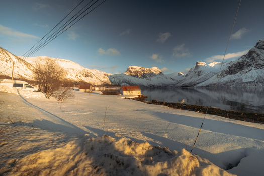 View of a serene winter landscape where the snow covered ground meets the still water reflecting the majestic snow capped mountains Indregård Troms Norway. View of a serene winter landscape where the snow covered ground meets the still water reflecting the majestic snow capped mountains Indregård Troms Norway.