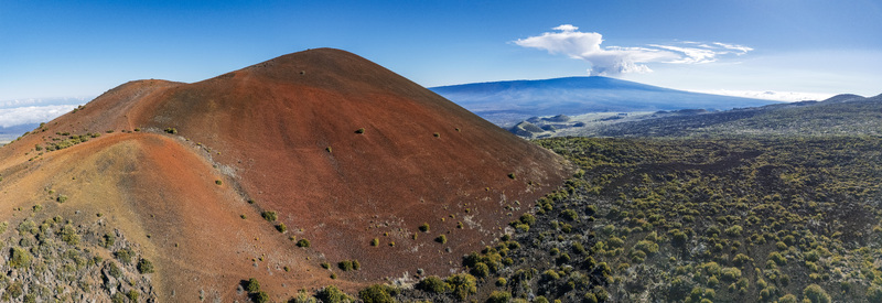 Aerial view of Mauna Kea featuring red volcanic cinder cones and rugged lava fields under a clear blue sky in Hawaii County Hawaii United States.