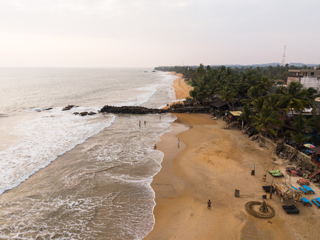 Aerial view of a sandy coastline with waves crashing on the shore palm trees and people relaxing on the beach under a hazy sky in Galle Southern Province Sri Lanka.