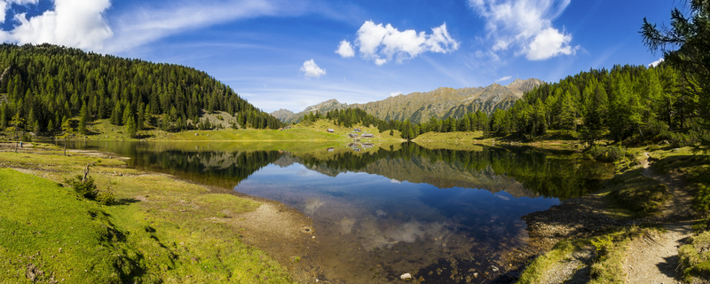 View of the tranquil lake mirroring the sky and surrounding green mountains with scattered huts under a blue sky with scattered clouds Duisitzkarsee Styria Austria. View of the tranquil lake mirroring the sky and surrounding green mountains with scattered huts under a blue sky with scattered clouds Duisitzkarsee Styria Austria.