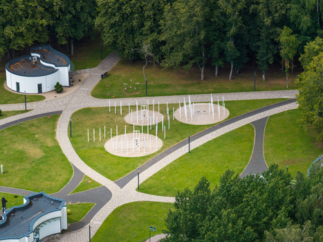 Aerial view of the sculpture park in Elektrenai featuring white vertical pillars in circular formations on green lawns with paved pathways and trees in Elektrenai Vilnius County Lithuania. Aerial view of the sculpture park in Elektrenai featuring white vertical pillars in circular formations on green lawns with paved pathways and trees in Elektrenai Vilnius County Lithuania.