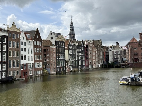 View of traditional canal houses and the Oude Kerk tower along the water under a cloudy sky in Amsterdam Netherlands. View of traditional canal houses and the Oude Kerk tower along the water under a cloudy sky in Amsterdam Netherlands.