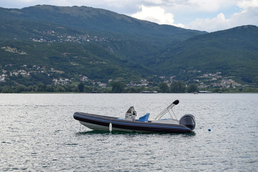 View of a rigid inflatable boat floating on the calm waters of Lake Ohrid with lush green mountains in the background in Ohrid Municipality of Ohrid North Macedonia. View of a rigid inflatable boat floating on the calm waters of Lake Ohrid with lush green mountains in the background in Ohrid Municipality of Ohrid North Macedonia.