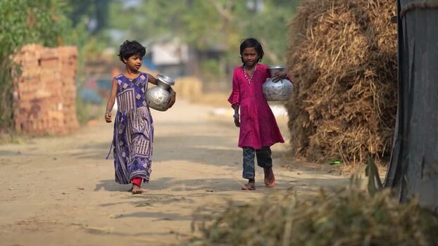 View of two girls carrying water pots on a rural path Bangladesh.