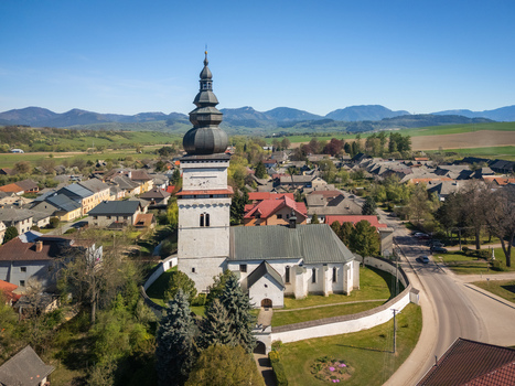 Aerial view of the historic Church of St. Matthew with its tall dark spire and white fortified wall overlooking the village rooftops and distant mountains in Partizanska Lupca Zilina Region Slovakia. Aerial view of the historic Church of St. Matthew with its tall dark spire and white fortified wall overlooking the village rooftops and distant mountains in Partizanska Lupca Zilina Region Slovakia.