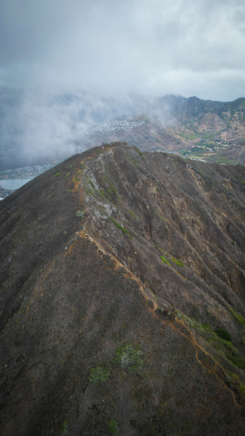 Aerial view of a steep trail snaking up the rugged arid slopes of Koko Head volcano contrasting with the soft enveloping clouds above Honolulu Hawaii United States. Aerial view of a steep trail snaking up the rugged arid slopes of Koko Head volcano contrasting with the soft enveloping clouds above Honolulu Hawaii United States.