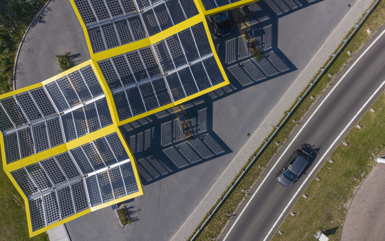 Aerial view of the Fastned charging station with its distinctive yellow solar panel canopy casting geometric shadows on the pavement next to a road in Lelystad Flevoland Netherlands. Aerial view of the Fastned charging station with its distinctive yellow solar panel canopy casting geometric shadows on the pavement next to a road in Lelystad Flevoland Netherlands.