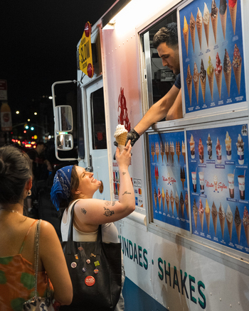 Brooklyn New York USA 14 June 2026 View of a woman purchasing an ice cream cone from a street vendor at night with the illuminated menu board and city lights in the background. Brooklyn New York USA 14 June 2026 View of a woman purchasing an ice cream cone from a street vendor at night with the illuminated menu board and city lights in the background.