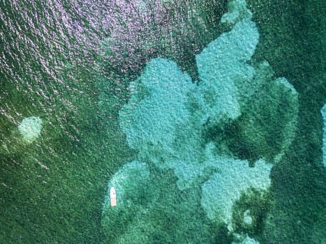 Aerial view of a small white boat floating on crystal clear turquoise water over coral reefs Guanaja Bay Islands Department Honduras. Aerial view of a small white boat floating on crystal clear turquoise water over coral reefs Guanaja Bay Islands Department Honduras.