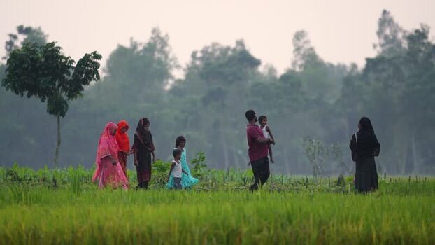 View of people walking through a green field in Bogura Bangladesh.