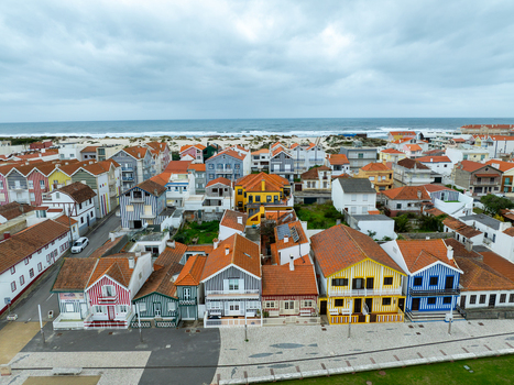 Aerial view of colorful houses with red and orange roofs meet sandy shores under a diffused sky Costa Nova Portugal.