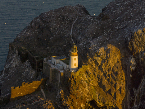 Aerial view of Bass Rock Lighthouse perched on the steep volcanic cliffs with nesting gannets under golden sunset light North Berwick Scotland United Kingdom. Aerial view of Bass Rock Lighthouse perched on the steep volcanic cliffs with nesting gannets under golden sunset light North Berwick Scotland United Kingdom.