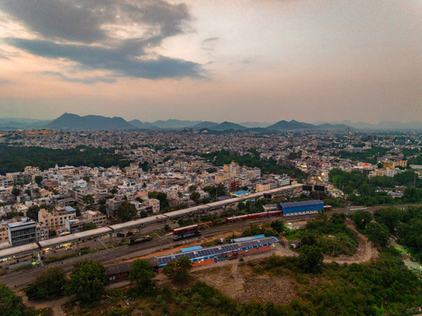 Aerial view of the dense urban landscape of Udaipur with railway tracks and distant mountains under a cloudy sky in Udaipur Rajasthan India. Aerial view of the dense urban landscape of Udaipur with railway tracks and distant mountains under a cloudy sky in Udaipur Rajasthan India.