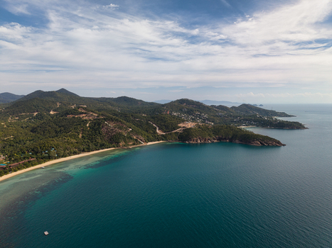 Aerial view of Ko Pha Ngan showing the coastline lush green hills turquoise waters and sandy beach under a blue sky with light clouds in Ko Pha ngan District Surat Thani Thailand.
