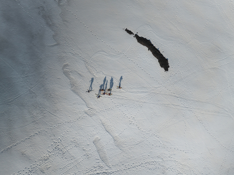 Aerial view of a group of skiers trekking across the snowy southern slope of Mount Etna with long shadows and tracks on the white surface Nicolosi Sicilia Italy. Aerial view of a group of skiers trekking across the snowy southern slope of Mount Etna with long shadows and tracks on the white surface Nicolosi Sicilia Italy.