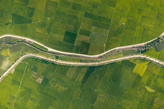 Aerial view of vibrant green rice paddies surrounding Lak Lake with a winding road and river cutting through the landscape in Lien Son Lak Dak Lak Vietnam. Aerial view of vibrant green rice paddies surrounding Lak Lake with a winding road and river cutting through the landscape in Lien Son Lak Dak Lak Vietnam.