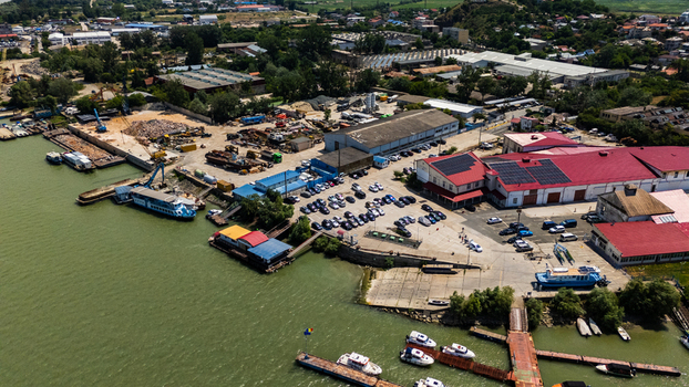 Aerial view of the industrial port area in Tulcea featuring warehouses with red roofs a parking lot filled with cars and various boats docked along the Danube river in Tulcea Tulcea Romania. Aerial view of the industrial port area in Tulcea featuring warehouses with red roofs a parking lot filled with cars and various boats docked along the Danube river in Tulcea Tulcea Romania.