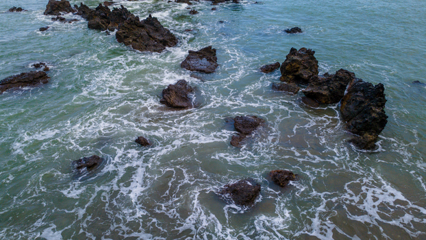 Aerial view of jagged dark rock formations in the turquoise sea with white foam from crashing waves at Pantai Karang Agung Ayah Central Java Indonesia. Aerial view of jagged dark rock formations in the turquoise sea with white foam from crashing waves at Pantai Karang Agung Ayah Central Java Indonesia.