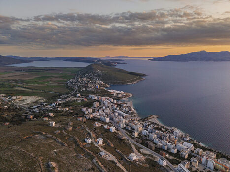Aerial view of the coastal city of Saranda featuring urban buildings rocky hills and the Ionian Sea coastline at sunset in Saranda Vlore County Albania. Aerial view of the coastal city of Saranda featuring urban buildings rocky hills and the Ionian Sea coastline at sunset in Saranda Vlore County Albania.