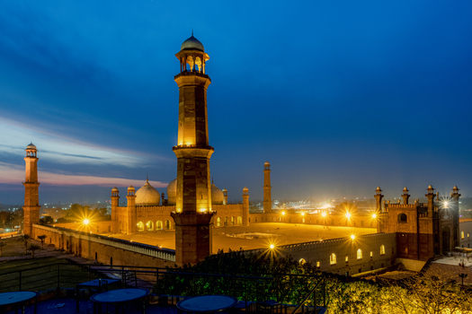 View of Badshahi Mosque at night with its illuminated minarets and domes glowing against a deep blue twilight sky in Lahore Punjab Pakistan. View of Badshahi Mosque at night with its illuminated minarets and domes glowing against a deep blue twilight sky in Lahore Punjab Pakistan.