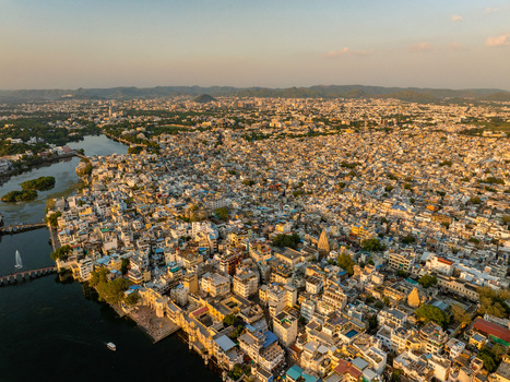 Aerial view of the historic city of Udaipur with its dense urban architecture and waterfront along Lake Pichola under the warm light of sunset in Udaipur Rajasthan India.