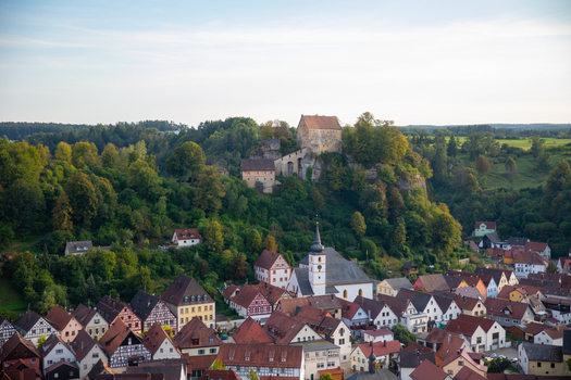 View of Pottenstein Castle perched on a rocky hill above the historic town with its half timbered houses and church tower Pottenstein Bavaria Germany.