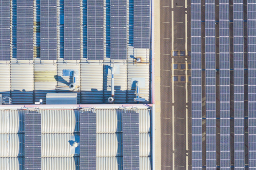 Aerial view of a large industrial building roof covered in rows of solar panels with ventilation units and corrugated metal surfaces in Arezzo Tuscany Italy. Aerial view of a large industrial building roof covered in rows of solar panels with ventilation units and corrugated metal surfaces in Arezzo Tuscany Italy.