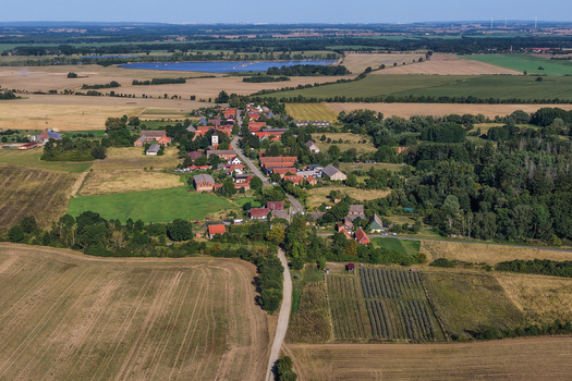 Aerial view of the village of Grimme featuring red roofed houses a historic church tower and surrounding agricultural fields and meadows in Bruessow Brandenburg Germany. Aerial view of the village of Grimme featuring red roofed houses a historic church tower and surrounding agricultural fields and meadows in Bruessow Brandenburg Germany.