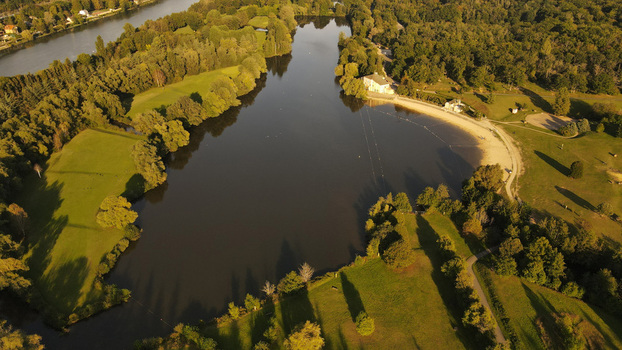 Aerial view of the lake in Chartrettes surrounded by lush green parkland trees and a sandy beach area under warm golden hour light in Chartrettes Ile de France France. Aerial view of the lake in Chartrettes surrounded by lush green parkland trees and a sandy beach area under warm golden hour light in Chartrettes Ile de France France.