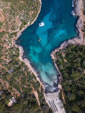 Aerial view of Cala Sa Nau cove with turquoise water a white catamaran and rocky cliffs in Felanitx Balearic Islands Spain. Aerial view of Cala Sa Nau cove with turquoise water a white catamaran and rocky cliffs in Felanitx Balearic Islands Spain.