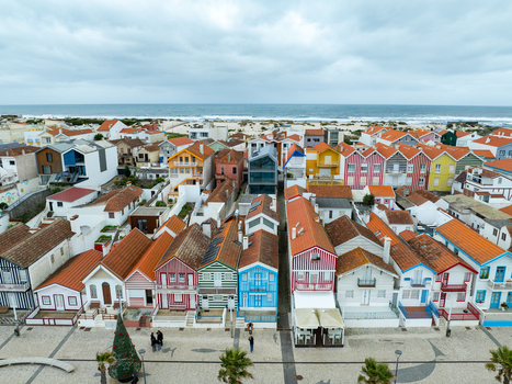 Aerial view of candy colored houses stand in neat rows against the backdrop of the Atlantic ocean Costa Nova Portugal.