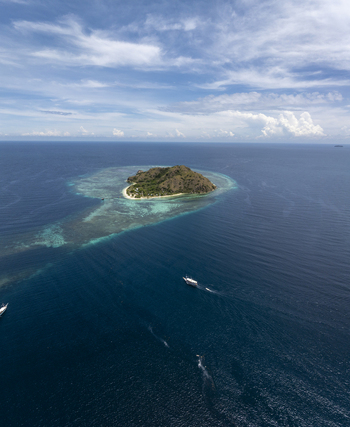 Aerial view of Kanawa Island surrounded by turquoise coral reefs and deep blue sea with boats in the distance Kecamatan Komodo Nusa Tenggara Timur Indonesia. Aerial view of Kanawa Island surrounded by turquoise coral reefs and deep blue sea with boats in the distance Kecamatan Komodo Nusa Tenggara Timur Indonesia.