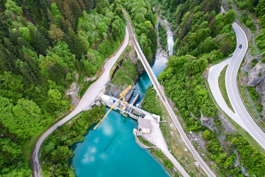 Aerial view of Lac du Vernex dam featuring a yellow crane railway bridge and turquoise water surrounded by lush green forest in Rossiniere Vaud Switzerland.