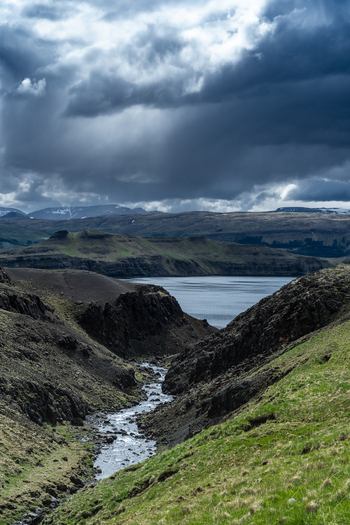 View of a stream flowing through a rocky valley towards the fjord under dramatic dark storm clouds in Hvalfjordur Iceland. View of a stream flowing through a rocky valley towards the fjord under dramatic dark storm clouds in Hvalfjordur Iceland.