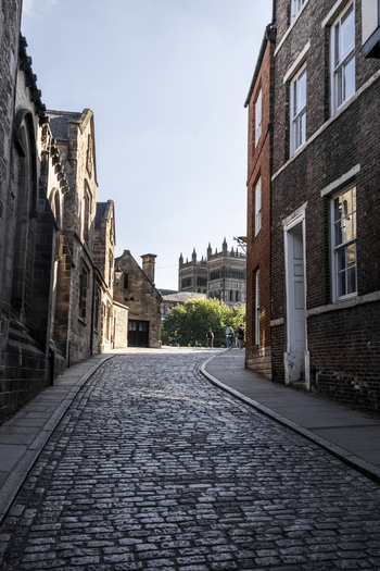 Durham England 13 July 2026 View of Durham Cathedral seen from a historic cobblestone street with brick buildings and pedestrians in the distance. Durham England 13 July 2026 View of Durham Cathedral seen from a historic cobblestone street with brick buildings and pedestrians in the distance.