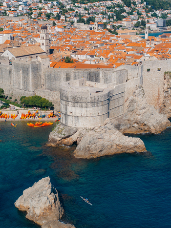 View of the historic stone walls and Bokar Fortress overlooking the turquoise Adriatic Sea with orange rooftops and kayaks on the shore in Dubrovnik Dubrovnik Neretva County Croatia. View of the historic stone walls and Bokar Fortress overlooking the turquoise Adriatic Sea with orange rooftops and kayaks on the shore in Dubrovnik Dubrovnik Neretva County Croatia.