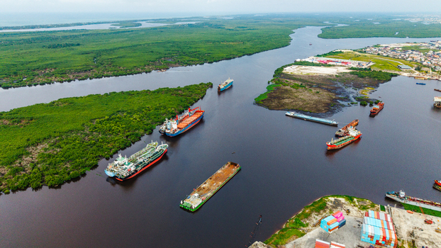 Aerial view of cargo ships and barges navigating the waterways near Satellite Town with lush mangrove forests and industrial port infrastructure in Lagos Lagos Nigeria.