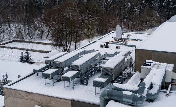 View of a snow covered rooftop featuring multiple HVAC units ventilation ducts and a satellite dish in Vilnius Vilnius County Lithuania. View of a snow covered rooftop featuring multiple HVAC units ventilation ducts and a satellite dish in Vilnius Vilnius County Lithuania.