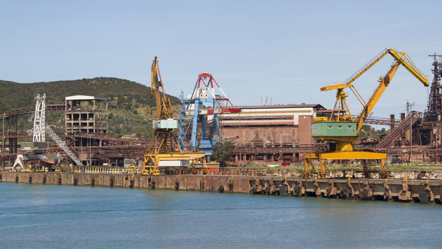 View of industrial cranes and aged ironworks stand in stark contrast to the calm turquoise sea under a clear sky Piombino Tuscany Italy. View of industrial cranes and aged ironworks stand in stark contrast to the calm turquoise sea under a clear sky Piombino Tuscany Italy.