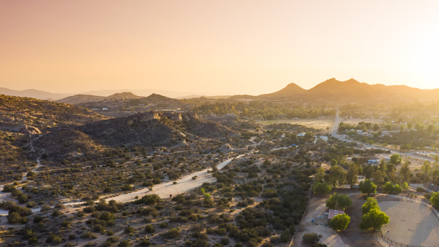 Aerial view of a desert landscape with rolling hills sparse vegetation a winding road and distant mountains under a warm sunset glow in the United States. Aerial view of a desert landscape with rolling hills sparse vegetation a winding road and distant mountains under a warm sunset glow in the United States.