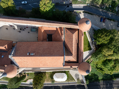 Aerial view of the historic Chateau de Grandson with its terracotta rooftops turrets and courtyard surrounded by greenery and nearby infrastructure in Grandson Vaud Switzerland.