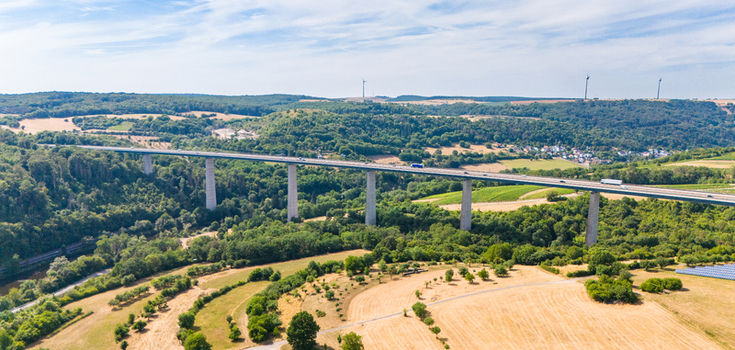 Aerial view of the Moselle bridge spanning the lush green Moselle valley with agricultural fields and wind turbines in the background in Langsur Rhineland Palatinate Germany.