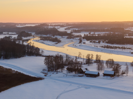 Aerial view of the snow covered Neris river valley and traditional wooden houses during a golden sunset in Kernave Vilnius County Lithuania.