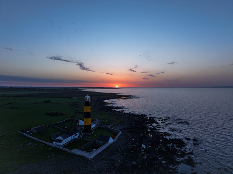 Aerial view of St John s Point Lighthouse standing on the rocky coastline during a vibrant sunset with green fields and the sea in Newcastle Northern Ireland United Kingdom. Aerial view of St John s Point Lighthouse standing on the rocky coastline during a vibrant sunset with green fields and the sea in Newcastle Northern Ireland United Kingdom.