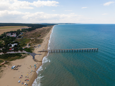 Aerial view of a long pier extending into the Black Sea at the sandy beach with surrounding coastal vegetation and clear blue water in Shkorpilovtsi Varna Bulgaria. Aerial view of a long pier extending into the Black Sea at the sandy beach with surrounding coastal vegetation and clear blue water in Shkorpilovtsi Varna Bulgaria.